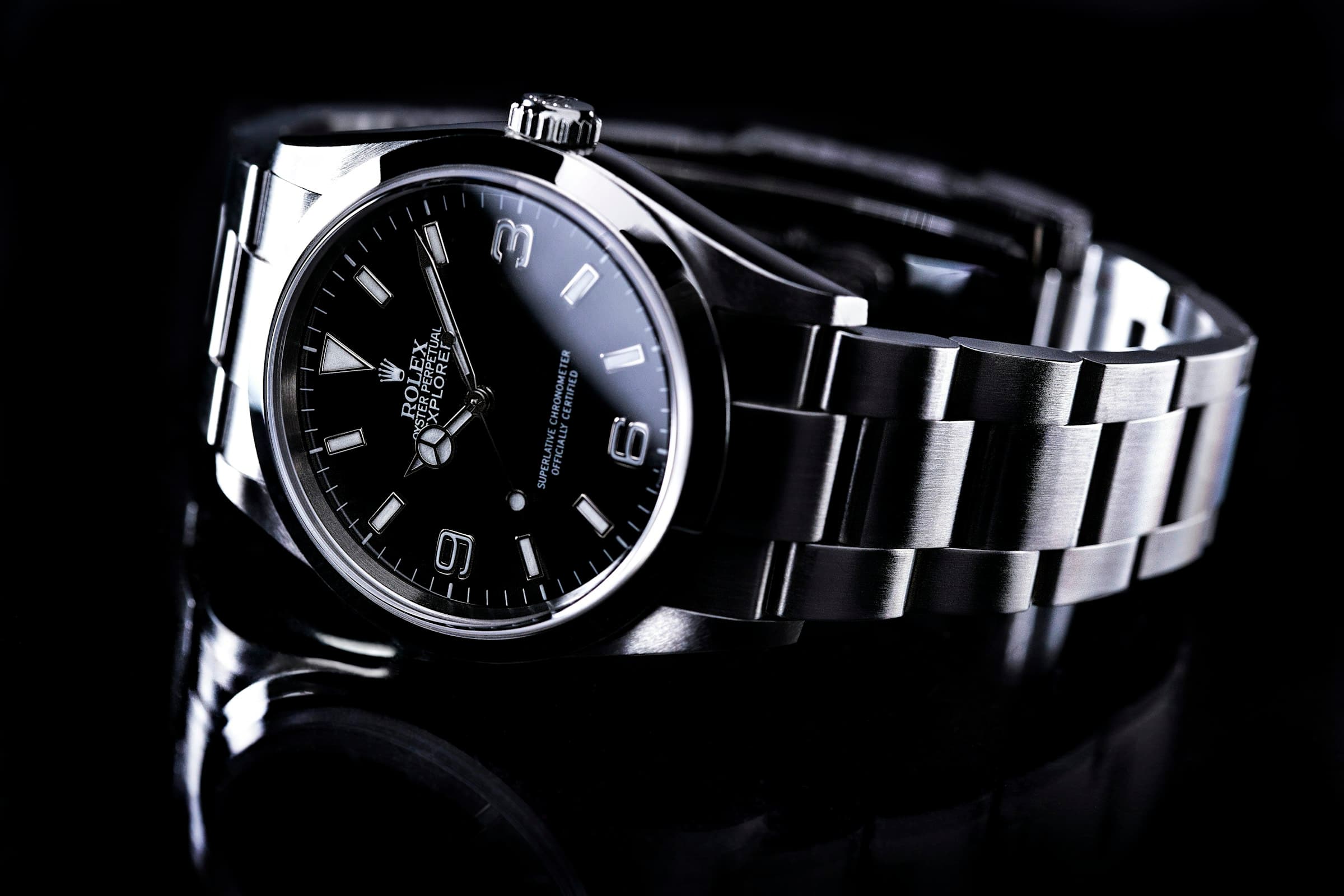 A steel sports watch on a black reflective surface